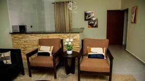 A living room with two brown armchairs, a small round table with a plant, and a stone wall. - GL Homez (Tanga)