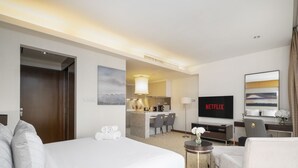 A hotel room with a bed, a desk, a TV, and a kitchenette.