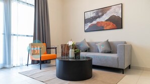 Een moderne woonkamer met een grijze bank, een oranje fauteuil, een zwarte salontafel en een groot abstract schilderij aan de muur.