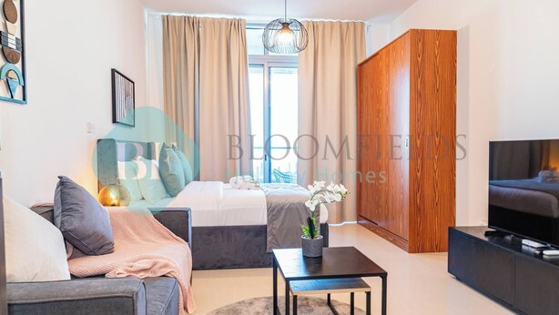 A modern bedroom with a bed, bedside table, and a TV. - Bloomfields Stylish STU in Julphar Al Reem (Abu Dabi)
