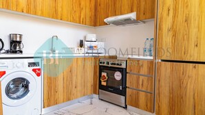 A compact kitchen with wooden cabinets, a washing machine, a microwave, and a built-in oven. - Bloomfields Spacious 2BR Duplex in Oasis Masdar (Abu Dabi)