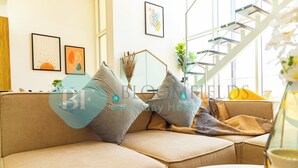 A modern living room with a beige sofa, a glass coffee table, and a staircase leading to an upper floor. - Bloomfields Spacious 2BR Duplex in Oasis Masdar (Abu Dabi)