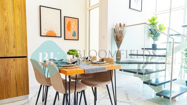 A modern dining area with a wooden table, chairs, and a glass staircase. - Bloomfields Spacious 2BR Duplex in Oasis Masdar (Abu Dabi)