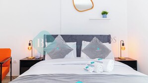 Een hotelkamer met een net opgemaakt bed, twee nachtkastjes met lampen, een spiegel aan de muur en een klein plankje met een plantje.