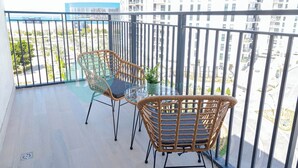Een balkon met rieten stoelen en een glazen tafel, met uitzicht op een stadslandschap met wolkenkrabbers.