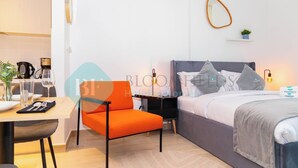 Een moderne hotelkamer met een bed, een bureau met stoel, een klein tafeltje en een plank met een plant.