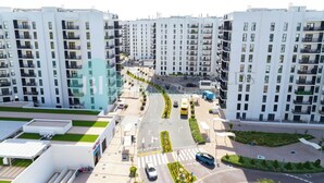 Ett modernt bostadskomplex med flera höga byggnader, en central gata med fordonstrafik och grönområden.