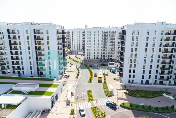 Um moderno conjunto de apartamentos com vários edifícios altos, uma rua central com veículos e áreas verdes.