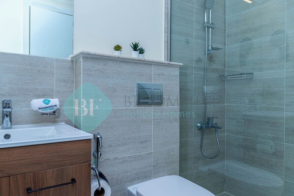 A modern bathroom with a shower, toilet, and sink. - Bloomfields Grandeur 2BR in Oasis Masdar City (Abu Dabi)