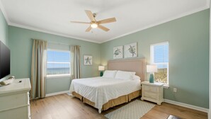 Une chambre à coucher comprenant un lit, des tables de chevet, un ventilateur de plafond, une commode et des œuvres d’art accrochées aux murs.