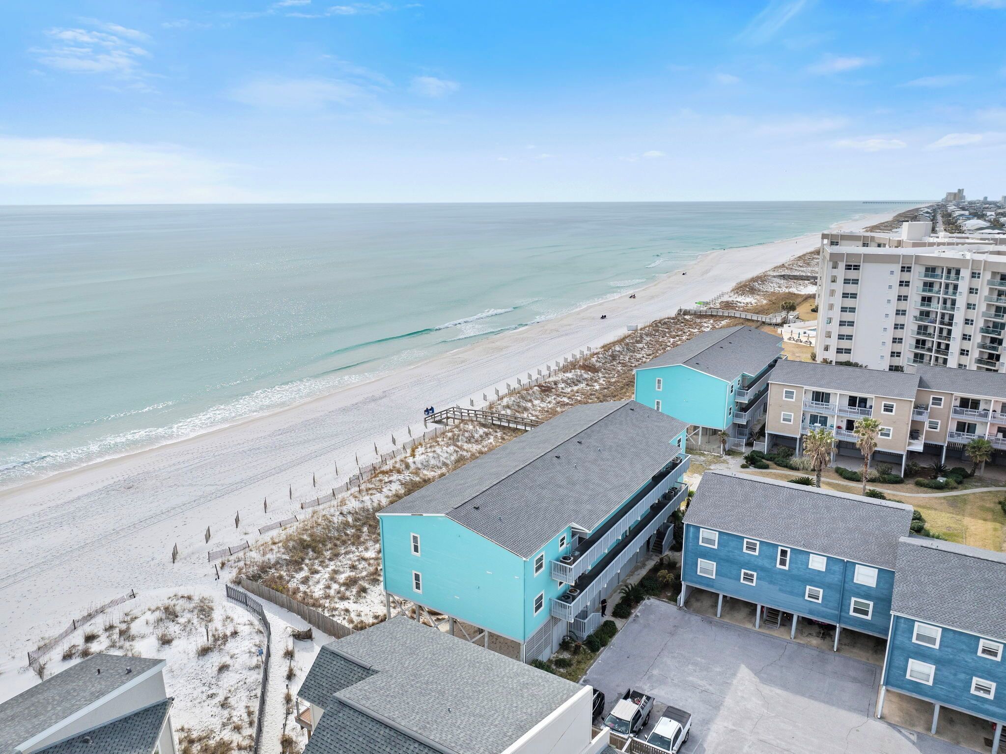 Un hotel costero con edificios de varios pisos, vista a la playa y un estacionamiento.