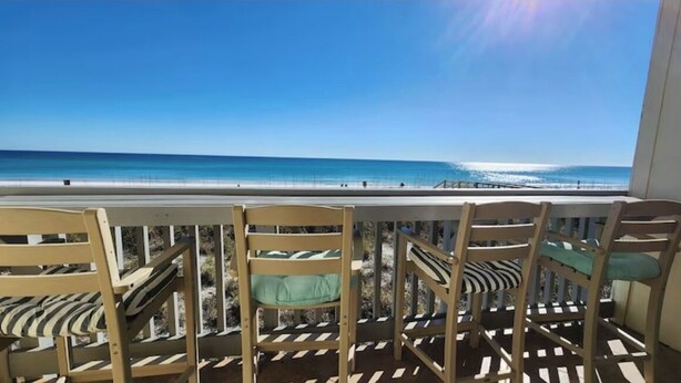 Une terrasse avec des chaises et une table en bois, donnant sur une plage aux eaux bleues et cristallines.