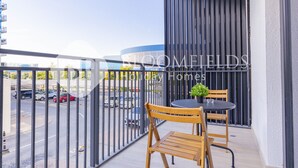 A balcony with a table and chairs, a potted plant, and a view of a parking lot with cars.