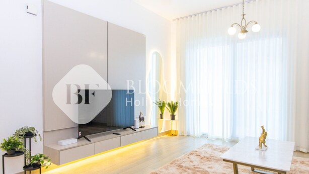 A modern living room with a large flat-screen TV mounted on a wall, a white table with a gold frame, a fluffy beige rug, and a potted plant on a side table.