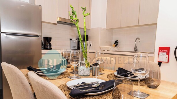 Une cuisine moderne avec une table à manger dressée pour deux personnes, agrémentée d’un vase avec des plantes vertes, de verres à vin et de couverts soigneusement disposés.