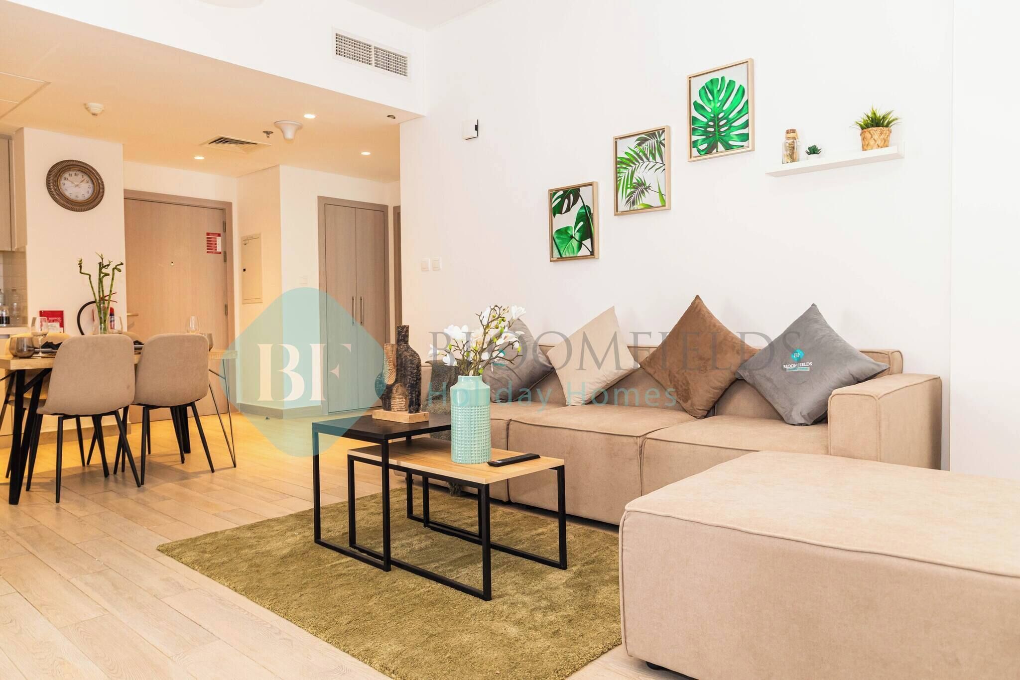 Een moderne woonkamer met een bank, salontafel en stoelen. Er hangt wanddecoratie en staat een klein plankje met planten.
