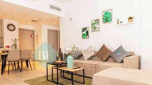 Un salon moderne avec un canapé, une table basse et des fauteuils. On y trouve des œuvres d’art murales et une petite étagère avec des plantes.