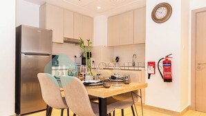 Une cuisine moderne avec un réfrigérateur en acier inoxydable, une table à manger en bois avec des chaises, un vase avec une plante et un extincteur fixé au mur.