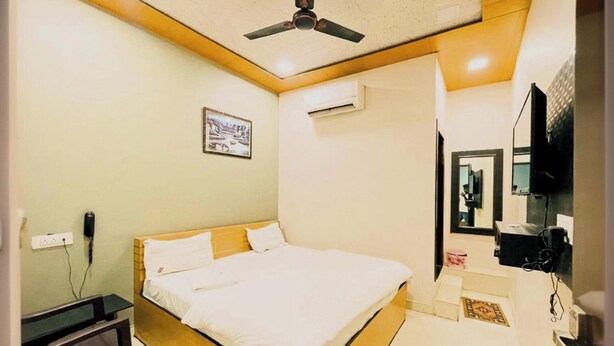 A bedroom with a bed, a desk, a ceiling fan, an air conditioner, a TV, and a framed picture on the wall. - Hotel Pragati Heights (Mathura)
