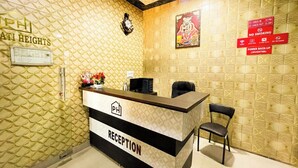 A reception desk with a 'PH' logo, a clock, and a 'RECEPTION' sign. There are two chairs and a small statue with flowers. - Hotel Pragati Heights (Mathura)