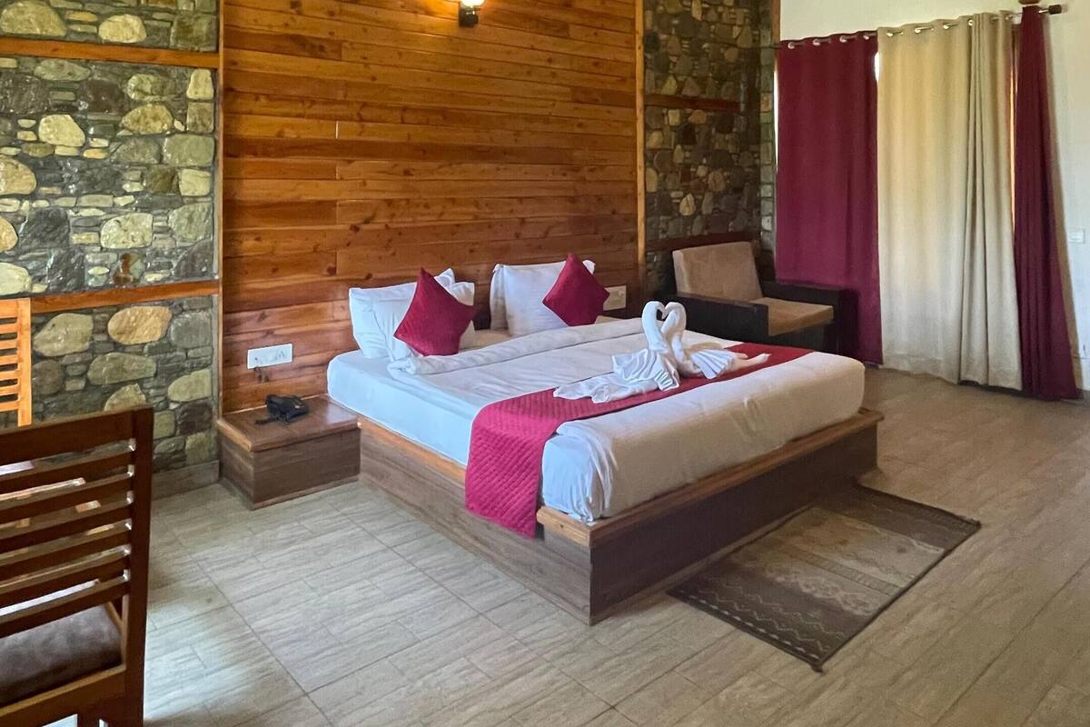 A spacious bedroom with a large bed, wooden ceiling, stone wall, and a ceiling fan.