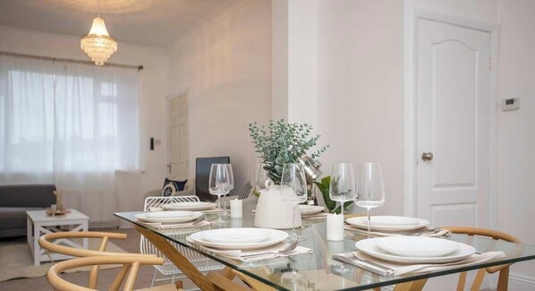 A dining area with a glass table set for four, white plates, and clear glasses. - Vacant Nests - The Melrose | Beach | Free Parking (Northumberland)