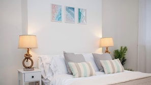 A neatly arranged bedroom with a bed, two bedside tables with lamps, a small drawer, and a potted plant. - Vacant Nests - The Melrose | Beach | Free Parking (Northumberland)