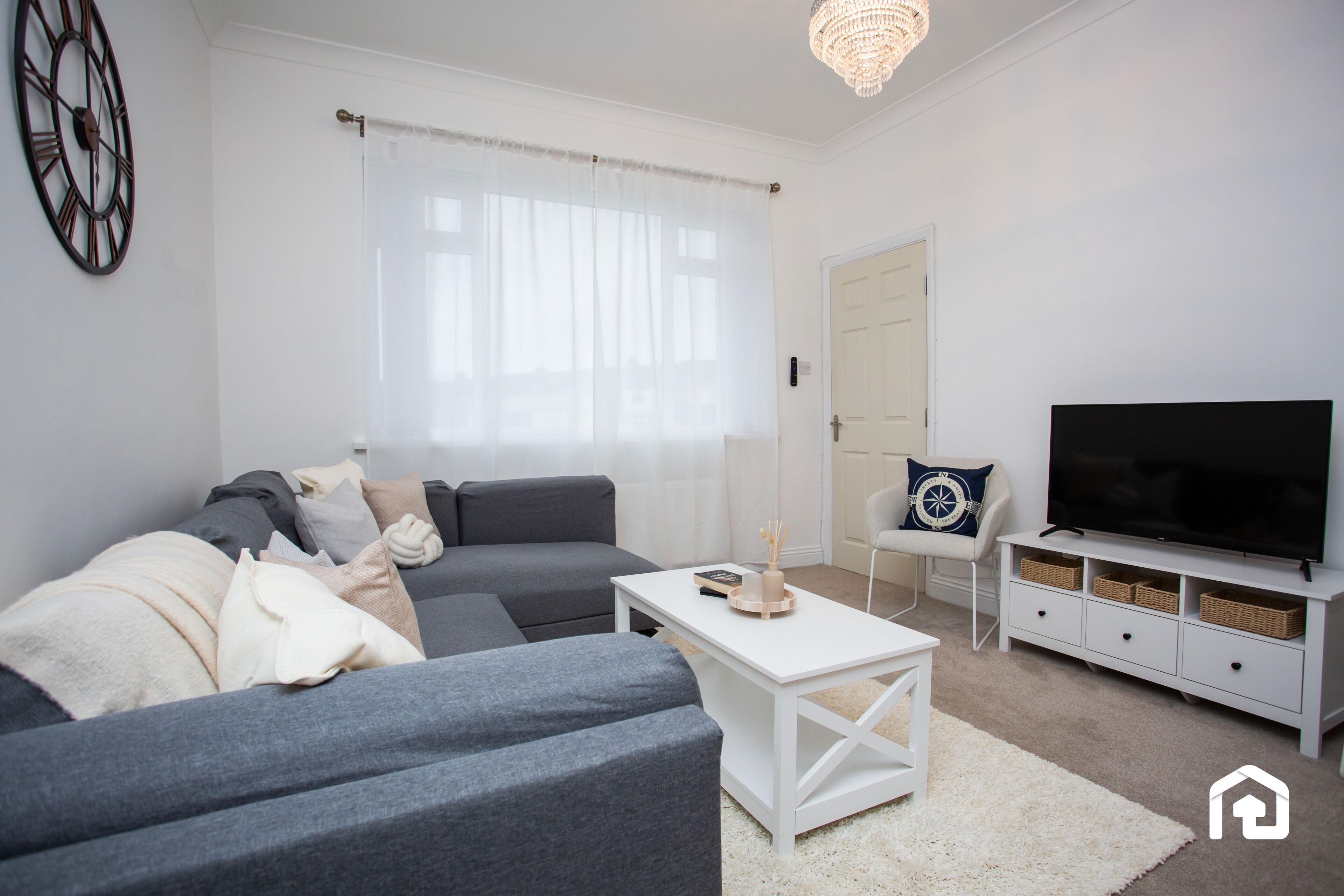 Relax in this bright, cozy living room featuring a comfy sectional sofa, soft neutral decor, and a flat-screen TV. The large window lets in plenty of natural light, creating a warm and inviting atmosphere.