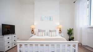 Ein Schlafzimmer mit einem weißen Babybett, zwei Nachttischen mit Lampen, einem Fernseher und gerahmten Bildern an der Wand.