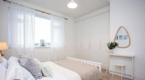 A bedroom with a bed, bedside table, and a window with curtains. - Vacant Nests - The Melrose | Beach | Free Parking (Northumberland)