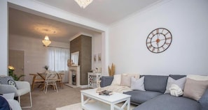 A living room with a sofa, coffee table, and a dining area with chairs and a table. - Vacant Nests - The Melrose | Beach | Free Parking (Northumberland)