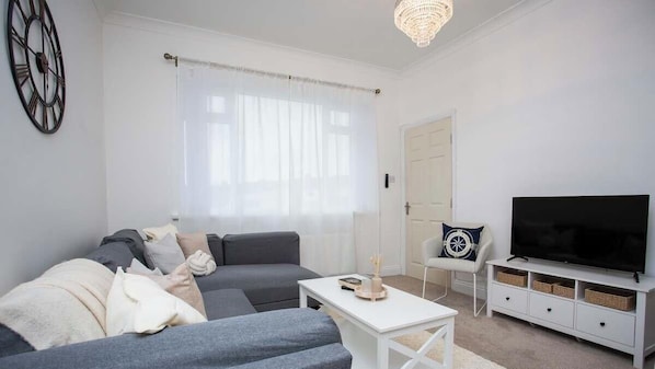 A modern living room with a sofa, TV, and a chandelier. - Vacant Nests - The Melrose | Beach | Free Parking (Northumberland)