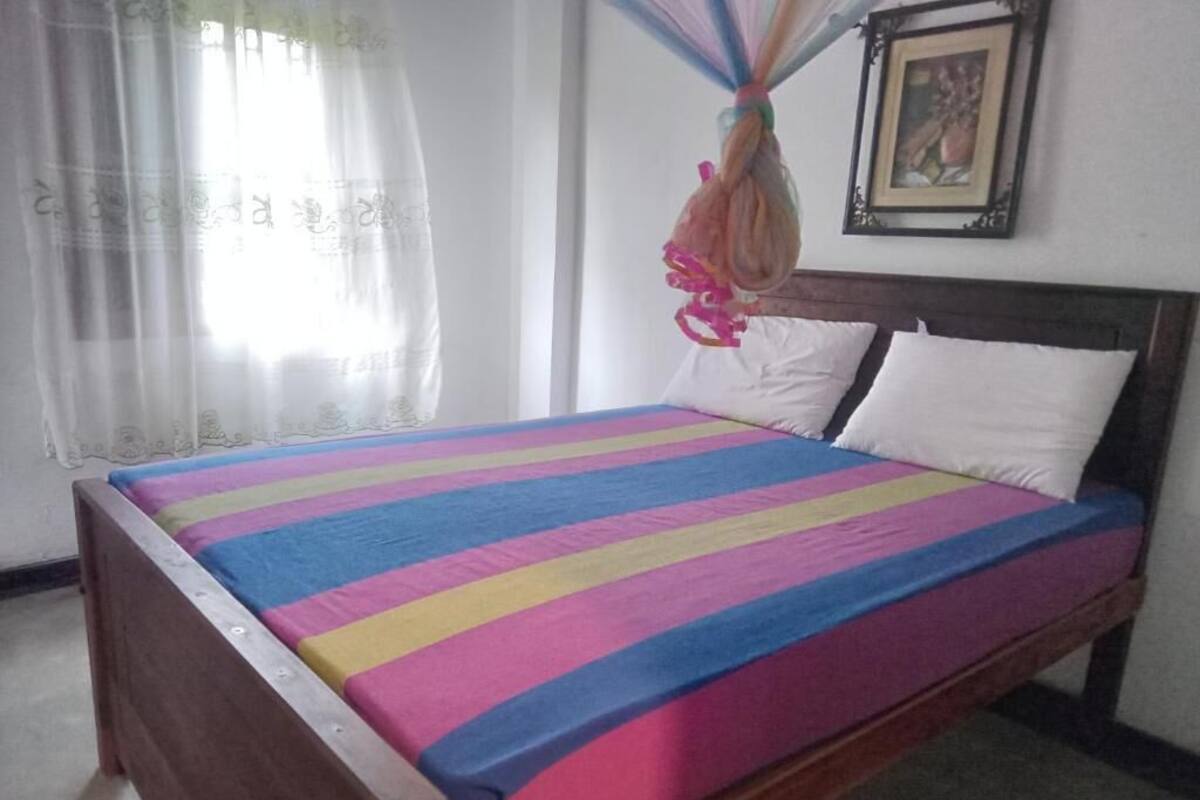 A bed with a colorful striped bedspread, a wooden headboard, white pillows, and a framed picture on the wall.