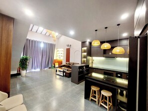 Une cuisine moderne dotée d’un îlot central, de tabourets de bar, de luminaires suspendus et d’un coin repas avec un canapé et des rideaux.