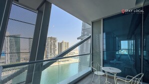 A balcony with a view of a river and buildings, furnished with white chairs and a table. - Summer 1BR Sanctuary l Central l Balcony Canal View l Downtown (Dubai)