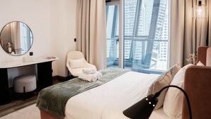 A hotel room with a bed, a desk, a chair, a round mirror, and a window with a city view. - Summer 1BR Sanctuary l Central l Balcony Canal View l Downtown (Dubai)