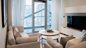A modern living room with a sofa, a coffee table, and a TV. There is a balcony with a view of buildings. - Summer 1BR Sanctuary l Central l Balcony Canal View l Downtown (Dubai)