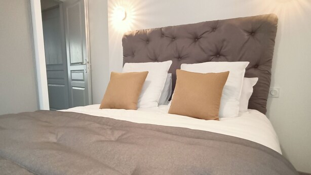 Una cama bien hecha con un cabecero capitonado, dos almohadas y una colcha gris.