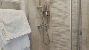 Zona de ducha con mampara de vidrio, toallero con toallas dobladas y cabezal de ducha.
