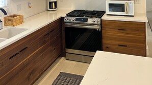 Eine moderne Küche mit Holzschränken, einem Edelstahlherd, einer Mikrowelle und einer Kaffeemaschine.