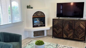 Ein Wohnzimmer mit Kamin, Flachbildfernseher, Deckenventilator und zwei sesselartigen Stühlen in Türkis.