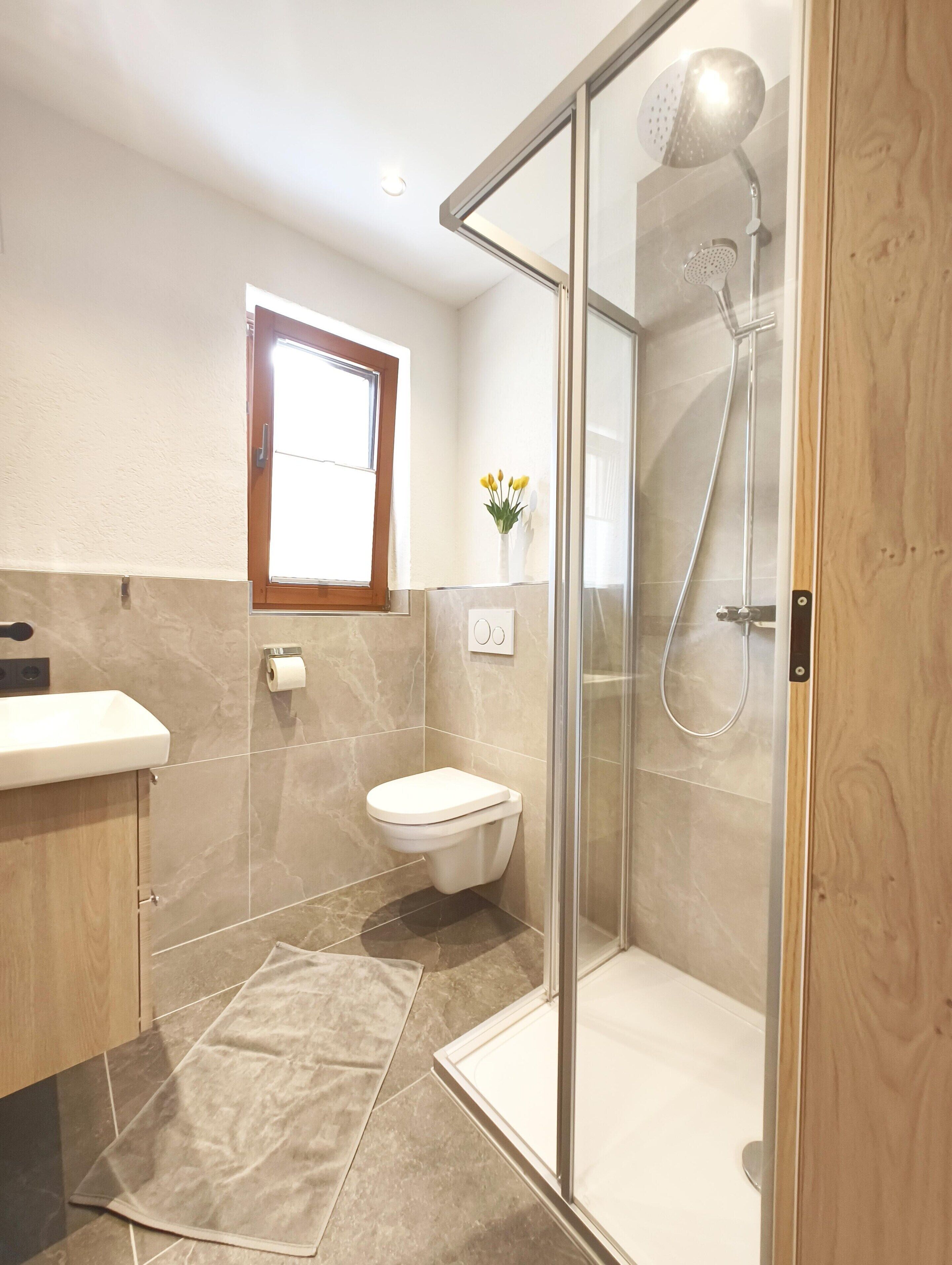 Een moderne badkamer met een douchecabine, een toilet en een wastafelmeubel met een raam boven de wastafel.