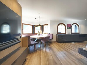 A modern living room with a large flat-screen TV, a dining area with a wooden table and chairs, and a built-in bench. - Exclusive Apartment With Garden and Whirlpool (Ramsau im Zillertal)