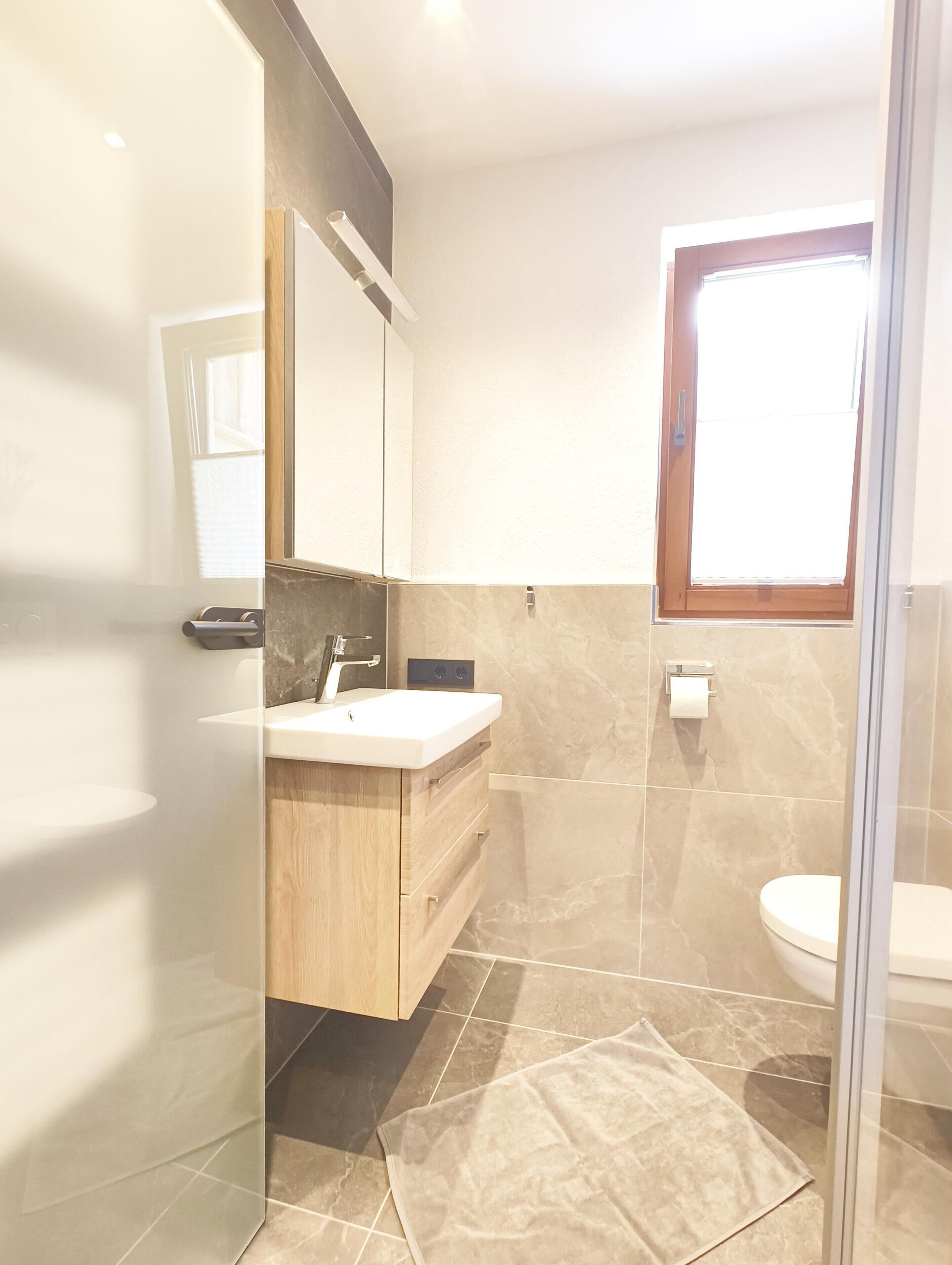 A modern bathroom with a glass shower enclosure, a wooden vanity, and a toilet.