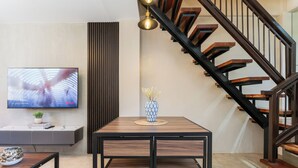 Una sala de estar moderna con una mesa de comedor de madera, un televisor instalado en la pared y una escalera con escalones de madera.