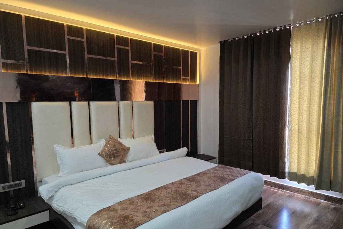 Habitació d'hotel moderna amb un llit gran, un capçal amb il·luminació integrada, una tauleta de nit i una finestra amb cortines.