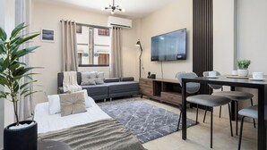 Ein modernes Hotelzimmer mit Bett, einer Couch, einem Schreibtisch mit Stühlen, einem Fernseher und einer Zimmerpflanze.