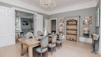 A traditional dining room with a table set for six, a chandelier, and a bookshelf.
