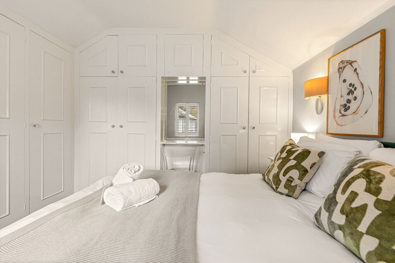 Een hotelkamer met een bed, een bureau en een stoel. Er liggen handdoeken op het bed en een lamp aan de muur.