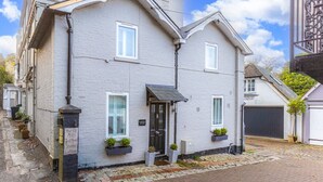 A two-story building with a black front door, white windows, and a small porch area with potted plants. - Mills Cottage - Sleeps 4 (Henley-On-Thames)